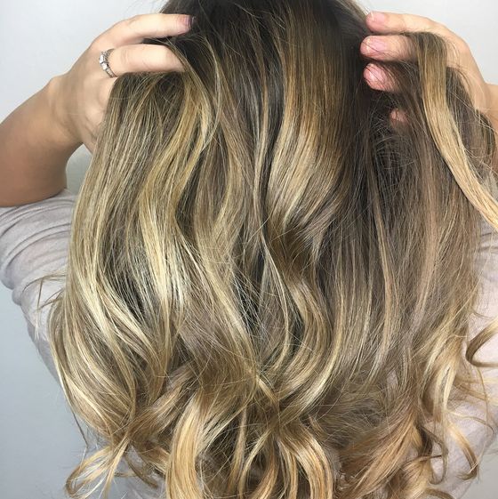 Hands lifting long, wavy hair with a dark root and bright blonde pieces