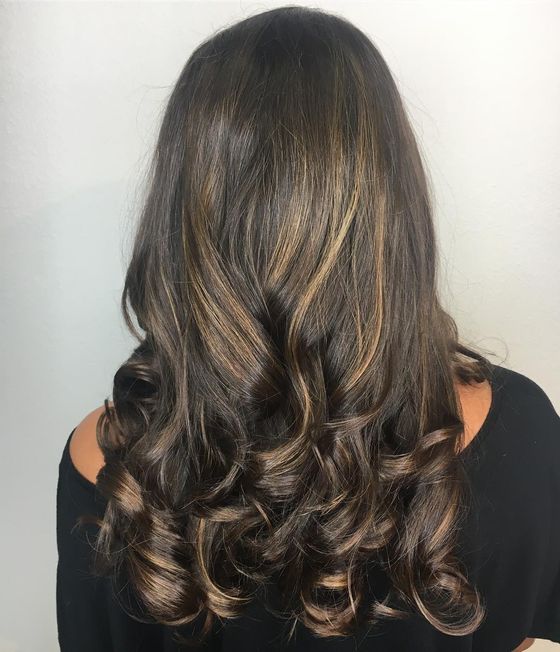 Long dark brown hair with caramel pieces, styled in bouncy curls