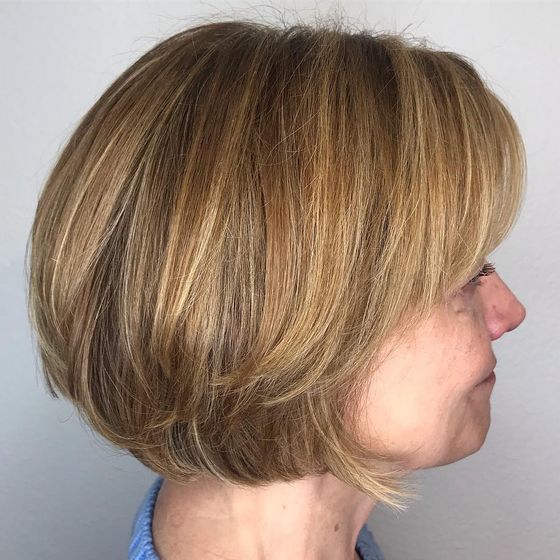 A rounded chin-length bob with bangs in warm golden brown with lighter pieces, in profile