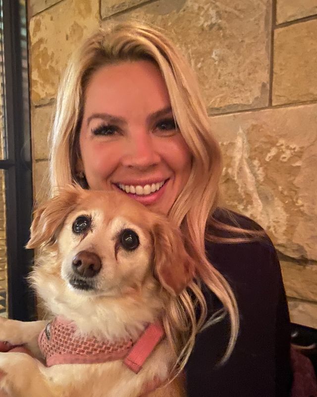 Lacie, smiling, with long blonde hair, holding a small tan and white dog